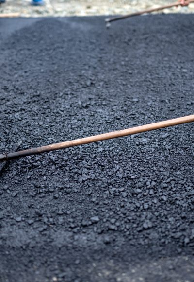 Worker leveling fresh asphalt on a road construction site, industrial buildings